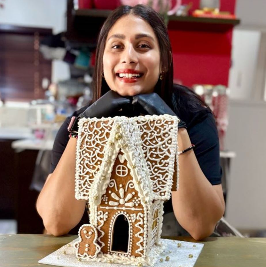 Rizwana Adams holding a beautifully decorated gingerbread house in her kitchen